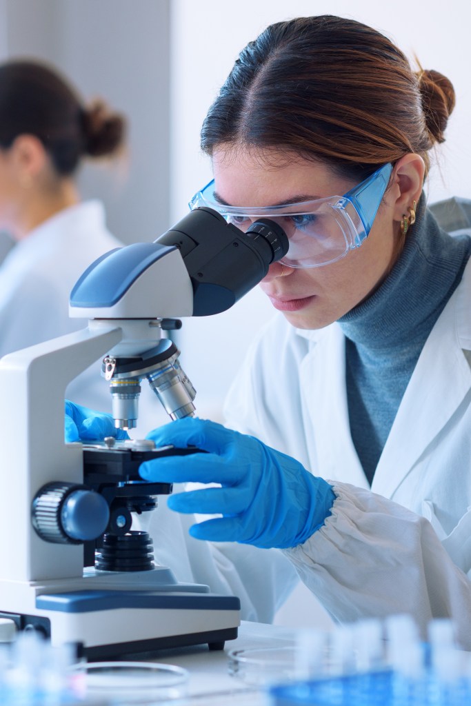 A researcher in a clinical laboratory looks through a microscope.
