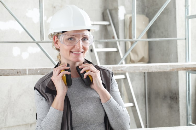 Female worker at a job site wearing hardhat and safety glasses and holding hearing protection