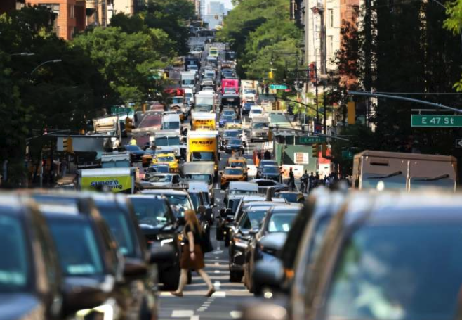 City traffic clogs a street in New York City as a pedestrian crosses.